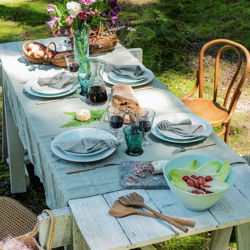 French country table setting with turquoise La Rochère glasses, wine carafe, blue plates, grey linen napkins and wooden cutlery
